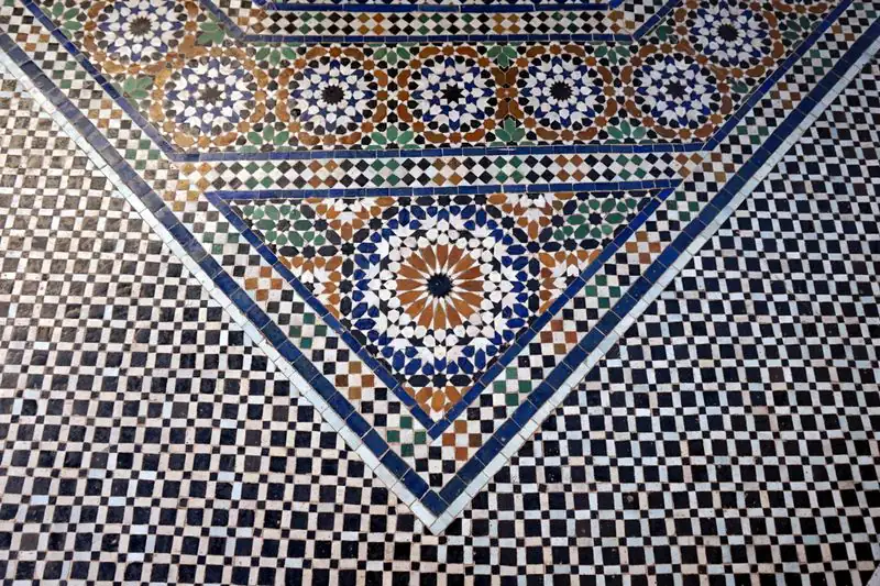 A zellige floor where a blue-edged chevron border with star medallions meets a field of small black and white squares.