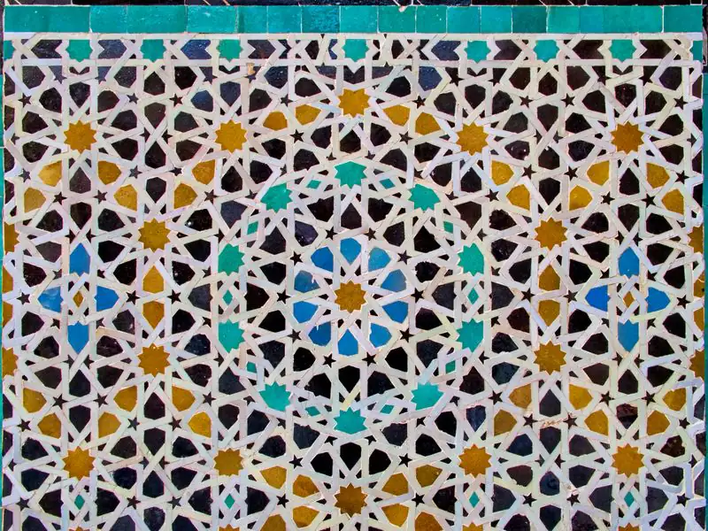 A dense field of zellige stars in ochre, blue, turquoise and black below a band of turquoise glazed tiles.