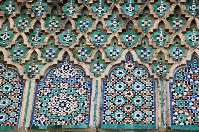 Turquoise, blue and white glazed tile set into raised, weathered arches on a historic facade.