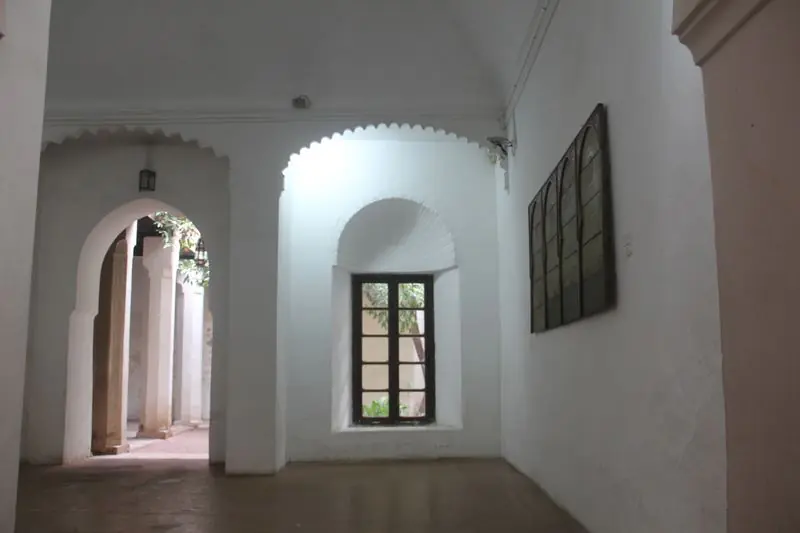 A white plastered room with arched openings, a deep-set window and a scalloped arch onto a bright courtyard.